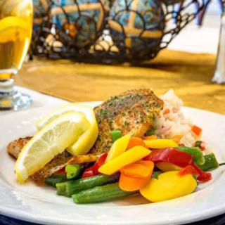 A gourmet dish featuring seasoned salmon with a side of colorful vegetables and lemon slices.