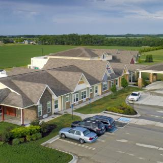 An aerial view of a building with adjacent parking lot and cars, set in a countryside landscape under a cloudy sky.