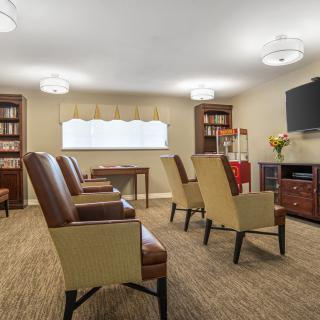A cozy seating area with several chairs, bookshelves, and a television mounted on the wall.