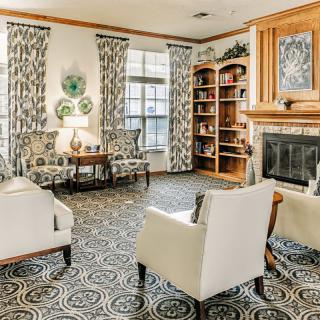 A cozy living room with armchairs and a fireplace, featuring a patterned carpet and decorative elements.