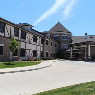 A large, two-story building with a modern architectural design and a circular driveway under a clear blue sky.