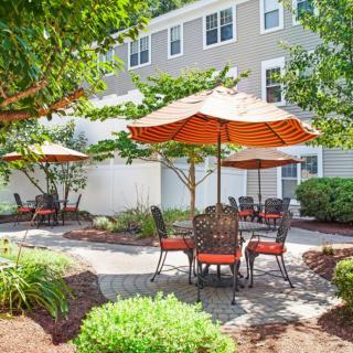 A charming outdoor patio area with tables and chairs under large umbrellas, surrounded by lush green landscaping.