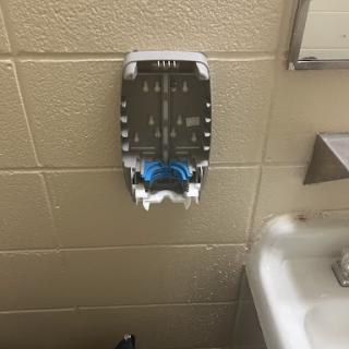 A wall-mounted soap dispenser in a bathroom, featuring blue accents.