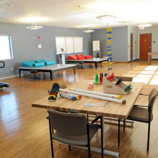 A spacious and brightly lit room designed for various activities, featuring tables, chairs, and colorful items.