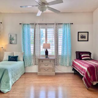A cozy and well-lit bedroom featuring two twin beds, bright blue curtains, and warm wooden flooring.