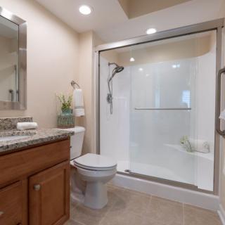 A modern bathroom featuring a glass-enclosed shower, toilet, and sink with a wooden cabinet.