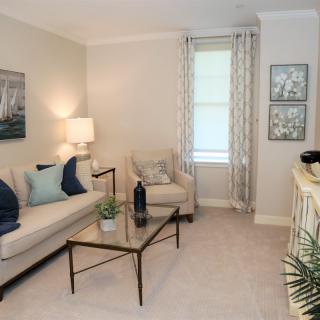 A cozy and elegantly decorated living room featuring a sofa, coffee table, lamp, and wall art.