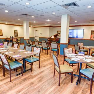 An empty restaurant dining area with neatly arranged tables and chairs, featuring wooden flooring and a piano in the corner.