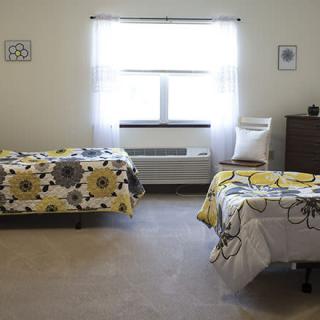 A neatly arranged bedroom featuring two twin beds with floral bedding, sunlight streaming through a window.
