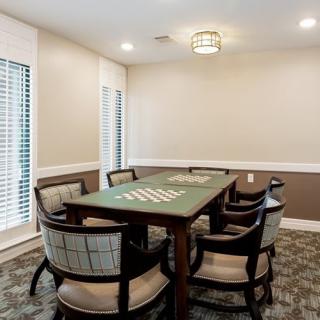 A well-lit dining room with a table and six chairs, featuring large windows and elegant decor.
