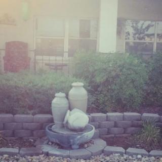 A serene garden fountain with decorative urns surrounded by lush greenery and a stone wall.