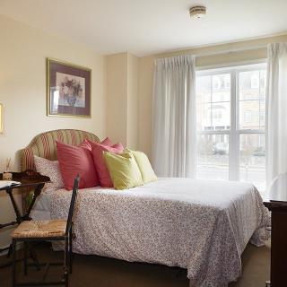 A cozy bedroom with a neatly made bed, colorful pillows, and natural light streaming through the window.