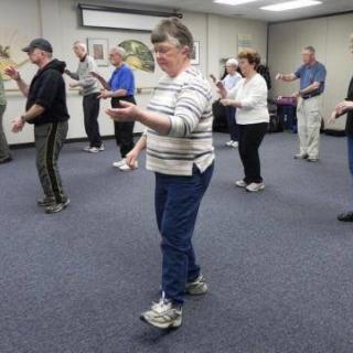 A group of people practicing Tai Chi in a classroom setting.