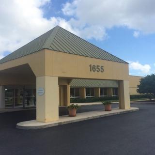 A commercial building entrance with a covered walkway and a parking lot in front.