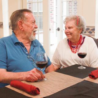 An elderly couple enjoying a conversation over wine at the dining table.