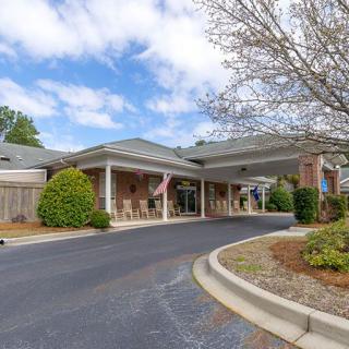 A building with a covered driveway, surrounded by trees and landscaping under a cloudy sky.