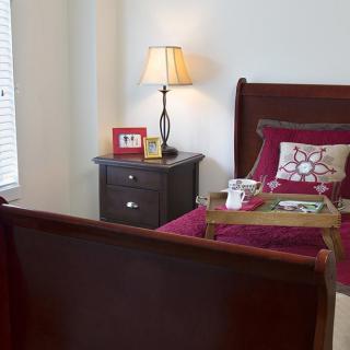 A cozy bedroom with a wooden bed, nightstand, and lamp, featuring a tray on the bed.