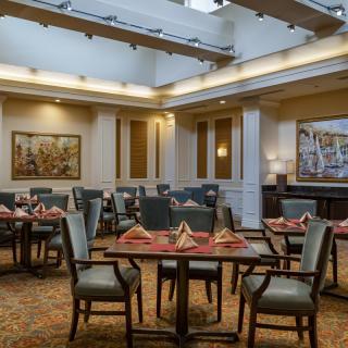 An elegantly set dining room with neatly arranged tables and chairs, surrounded by artwork on the walls.