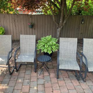Four patio chairs and a table with a potted plant in a garden setting.