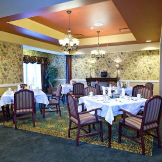 A well-decorated dining room with neatly arranged tables and chairs, featuring elegant lighting and floral wallpaper.