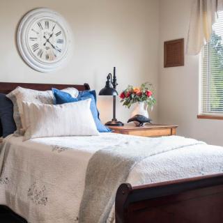 A cozy bedroom with a neatly made bed, decorative pillows, and a wooden nightstand beside a window.