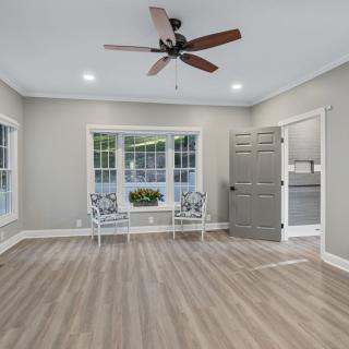 A modern living room with wood flooring, a ceiling fan, and large windows.