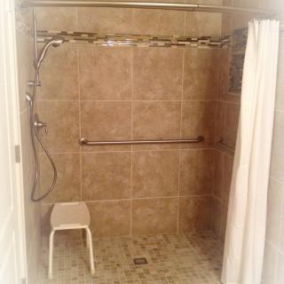 An accessible bathroom shower with a grab bar, curtain, and shower chair.