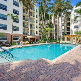 A luxurious apartment complex with a large outdoor swimming pool surrounded by palm trees.