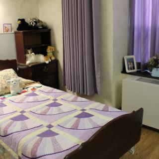 A cozy bedroom featuring a neatly made bed with a colorful quilt, complemented by soft curtains and minimalistic decor.