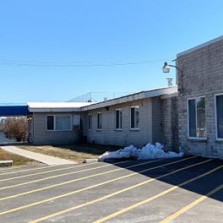 A modest brick building surrounded by a clear blue sky, featuring a parking area with some leftover snow.