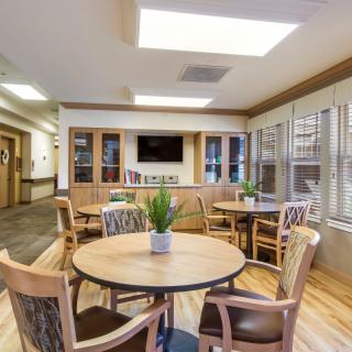 A cozy community seating area with tables and chairs, featuring a television and decorative plants.