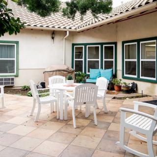A cozy patio with white outdoor furniture and plants against a home's exterior.