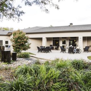 A serene outdoor patio area with tables and chairs, surrounded by greenery and a modern building in the background.