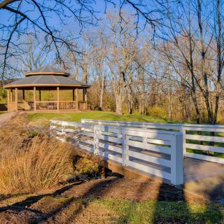 A serene park scene with a white bridge leading to a wooden gazebo surrounded by trees.