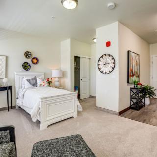 A cozy and elegantly designed bedroom featuring a white bed, decorative wall art, and a large clock.