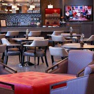 A modern restaurant interior featuring a dining area with tables and chairs, a television on the wall, and a bar in the background.