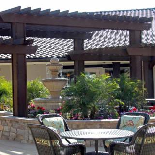 A beautifully landscaped patio area with a pergola, seating, a fountain, and lush greenery.