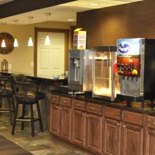 A cozy concession area with a popcorn machine and soda dispenser, featuring wooden cabinets and bar stools.