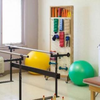 A physical therapy room equipped with parallel bars, stability balls, and various exercise tools.