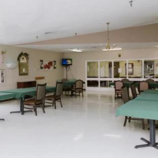 An empty dining area with green tablecloth-covered tables and chairs, featuring a TV and mirrors on the wall.