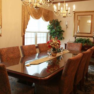 Elegant dining room with a large table, cushioned chairs, and chandeliers.