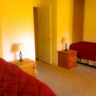 A cozy bedroom with two beds, each covered with red quilts, and nightstands with lamps.