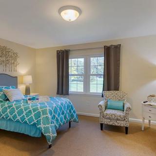 A cozy bedroom with a patterned bedspread, an upholstered chair, and ample natural light from the window.