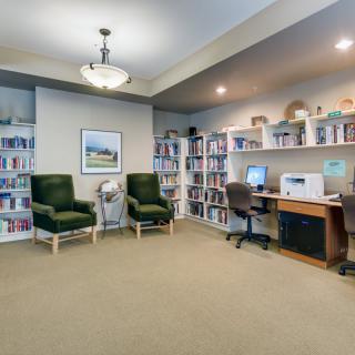 A cozy library reading area with bookshelves, comfortable chairs, and a computer desk.