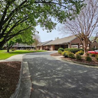 A suburban building with a driveway, surrounded by trees and landscaped gardens.