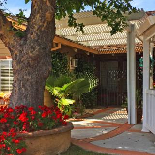 A charming garden entrance with a tree, vibrant flowers, and a pathway leading to the house.