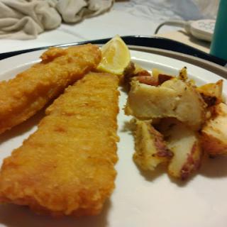 A delicious plate of fried fish fillets served with golden roasted potatoes and a slice of lemon.