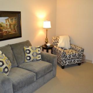 A cozy living room with a gray couch, patterned armchair, and soft lighting.