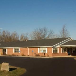 A brick residential building with a driveway and trees in the background under a clear sky.