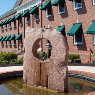 A stone sculpture fountain in front of a brick building with green awnings.